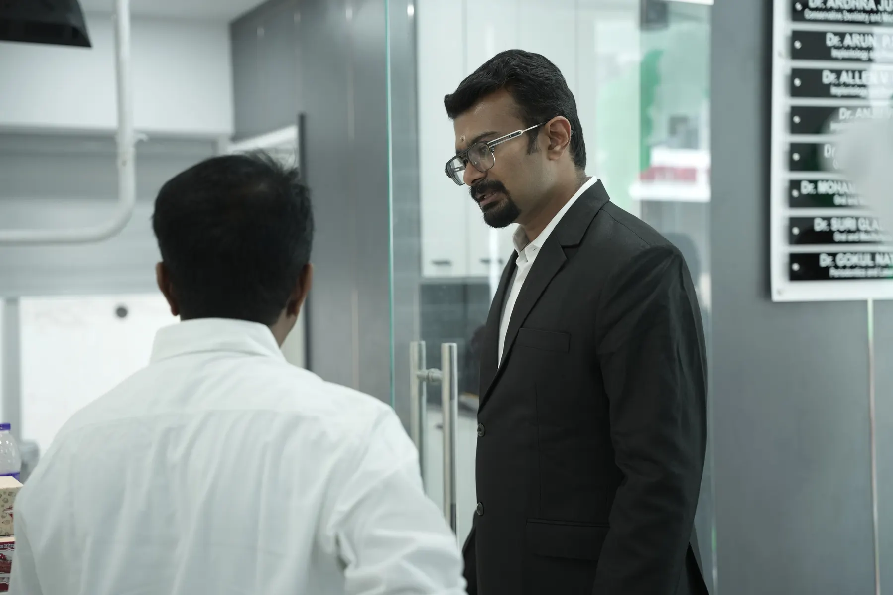 Dentist speaking with a visitor beside the doctors' name board at Dental Craft Vanchiyoor
